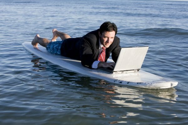 Person laying on a surfboard in the ocean using a laptop