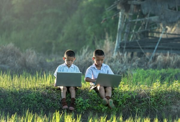 2 children sitting in the grass with their laptops