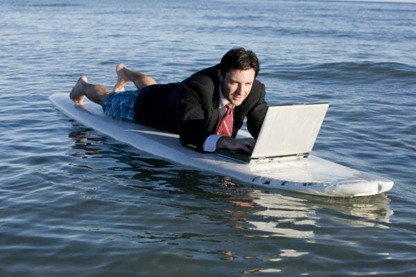 Man working on a laptop on a surfboard in the ocean